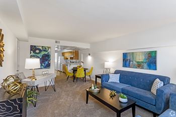 a living room with a blue couch and yellow chairs and a dining room table at The Fields of Bethesda, Maryland